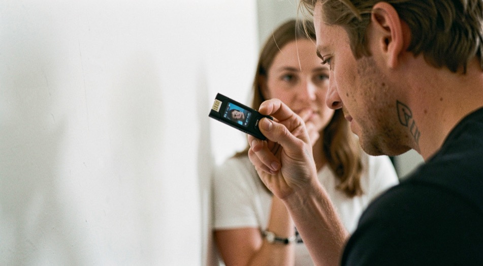 A photographer tilting a compact flash toward a white wall while a subject waits in soft side light