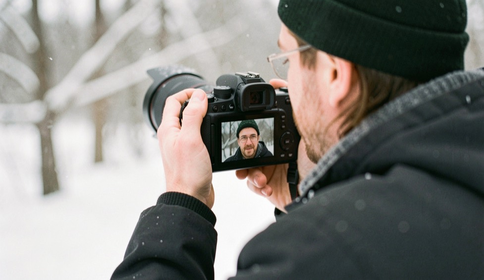 A photographer checking a bright winter portrait on a camera in soft snowy daylight with the rear screen turned away