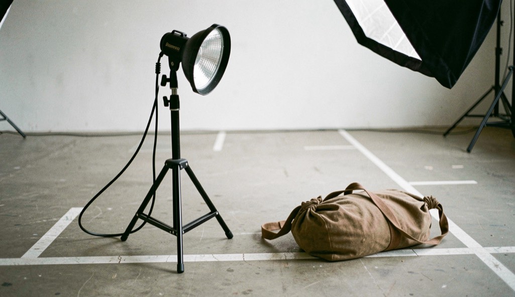 A compact studio kit with one light, softbox, stand, reflector and sandbag on a marked floor