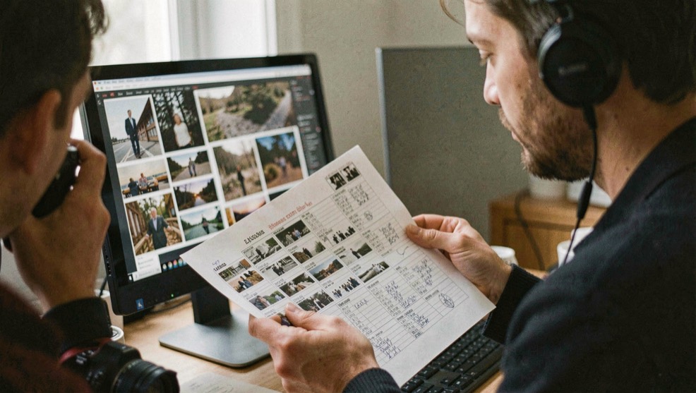 A photographer reviewing a contact sheet and export checklist beside a calibrated monitor
